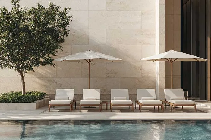 Row of pale loungers and umbrellas beside a swimming pool.